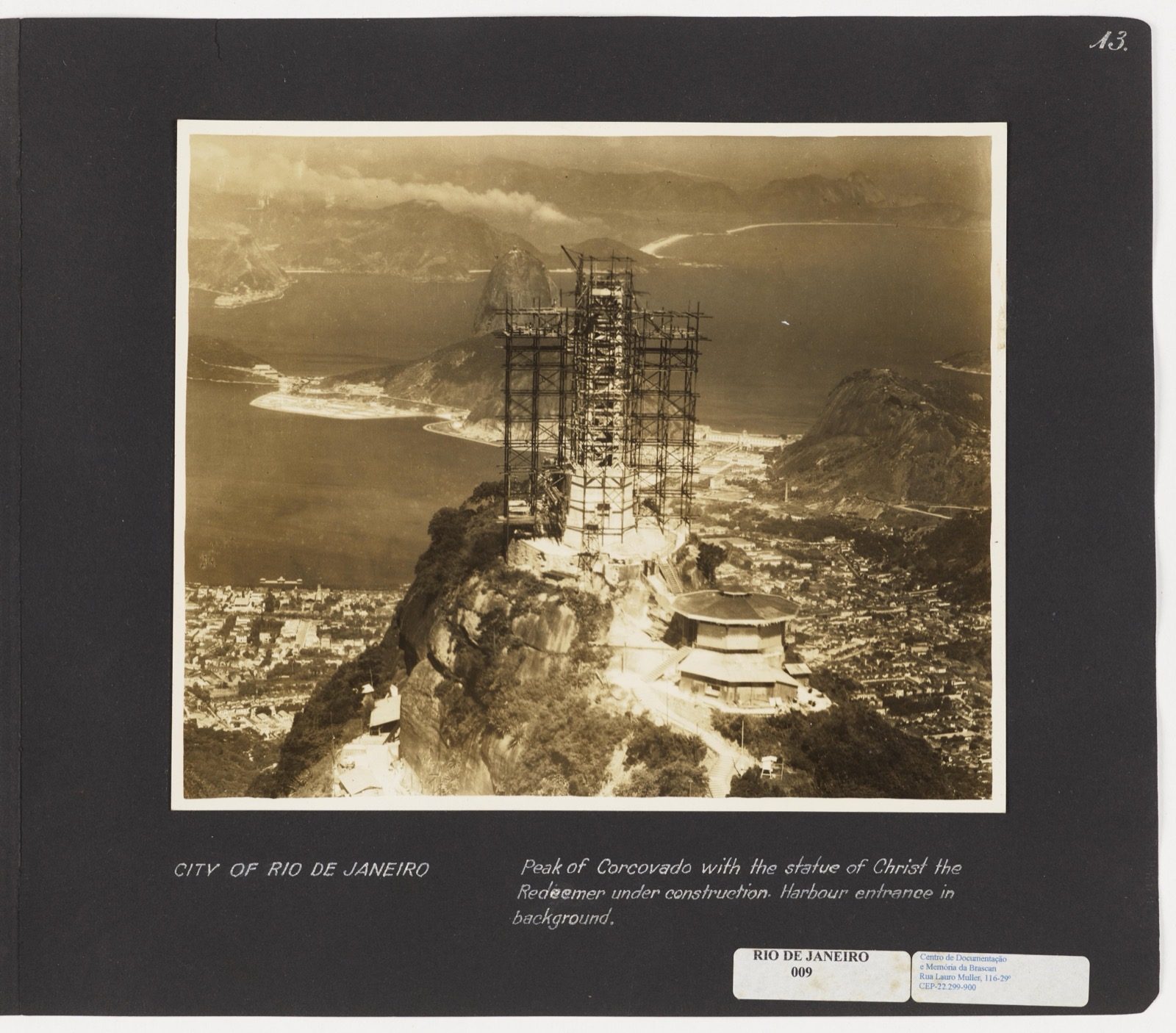 Black-and-white photograph from around 1930 showing the Christ the Redeemer statue mid-construction on Corcovado mountain, with scaffolding around the unfinished concrete torso and one arm still incomplete against the sky.