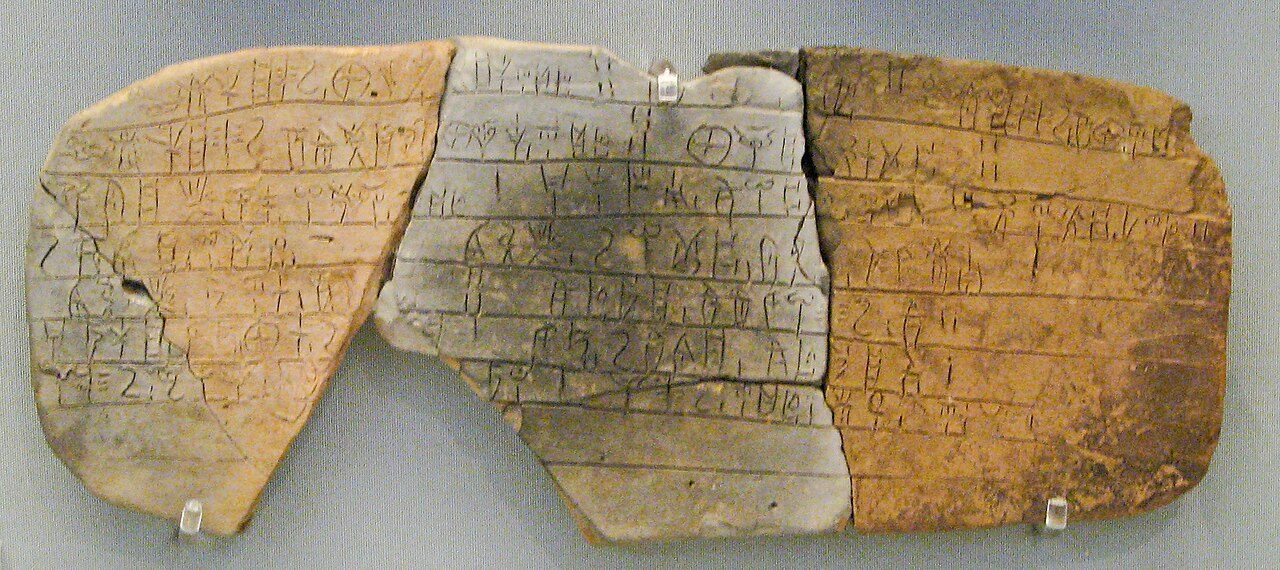 A Linear B clay tablet from the Mycenaean palace at Pylos on display at the National Archaeological Museum of Athens, showing rows of incised syllabic signs.