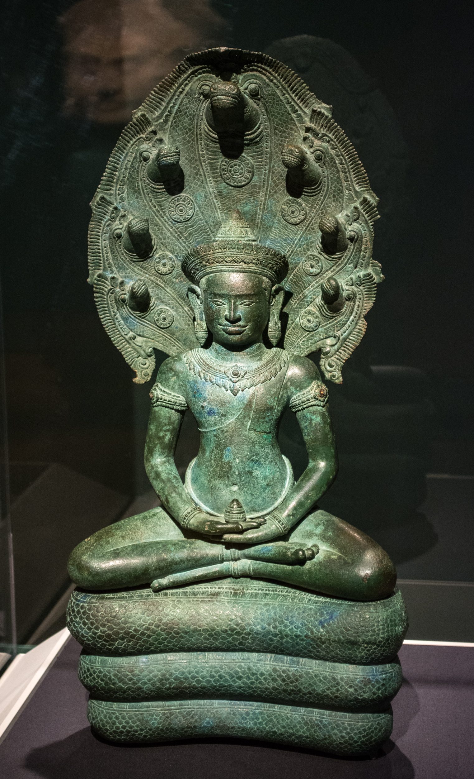 A bronze Buddha seated on the coils of the naga king Mucalinda, its multi-headed hood fanned out behind the Buddha's head, Cambodia, Angkor period, about 1100 CE.
