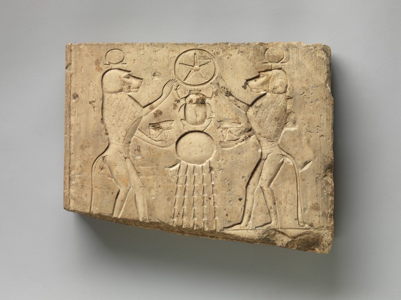 Ancient Egyptian relief panel, Late Period to Ptolemaic Period, showing two baboons offering the wedjat eye to the sun god Khepri, who holds the hieroglyphic sign for the underworld.