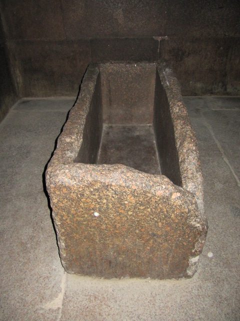 The empty granite sarcophagus in the King's Chamber of the Great Pyramid, standing on the floor of a granite-lined room whose walls carry no inscriptions or decoration.