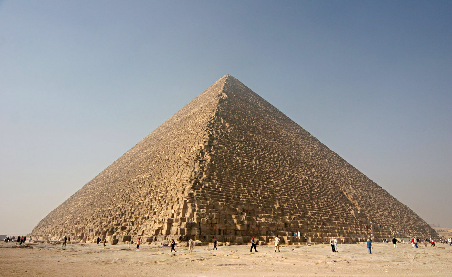 The Great Pyramid of Giza photographed from ground level against a clear blue sky, its stepped limestone blocks visible in daylight.