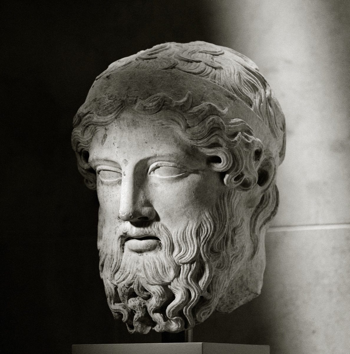 A weathered Roman-era marble head from a herm, a bearded pillar-statue of Hermes once used to mark boundaries, doorways, and crossroads across the Greek and Roman world.