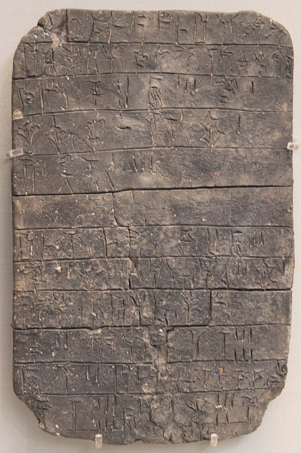 Linear B clay tablet Un 718 from the palace at Pylos, 13th century BC, ruled into lines and columns of syllabic signs recording offerings made to Poseidon. Tablets like this are palace accounting records, baked hard by the fire that destroyed the building, not religious texts.